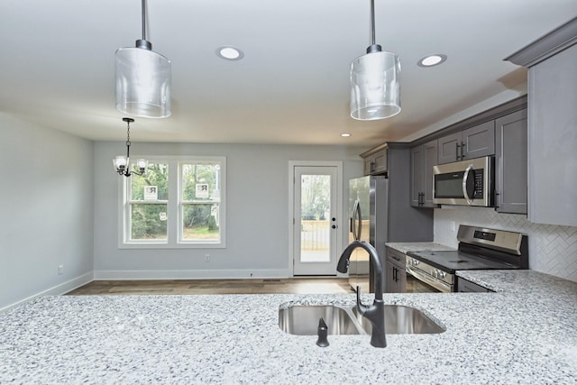 kitchen with sink, stainless steel appliances, tasteful backsplash, pendant lighting, and a chandelier