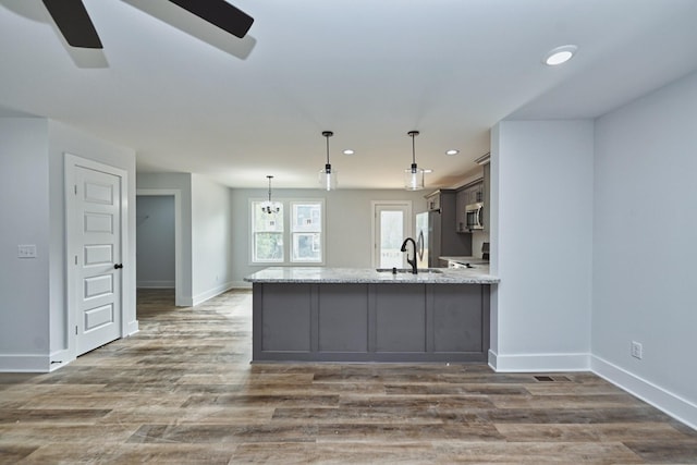 kitchen featuring kitchen peninsula, light stone counters, stainless steel appliances, decorative light fixtures, and dark hardwood / wood-style floors