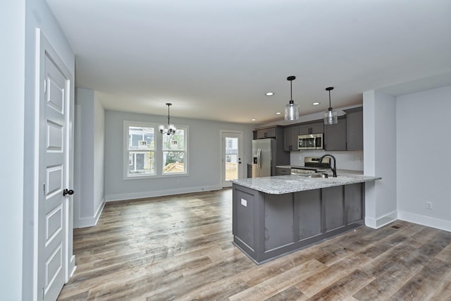 kitchen featuring light stone countertops, kitchen peninsula, tasteful backsplash, stainless steel appliances, and a chandelier