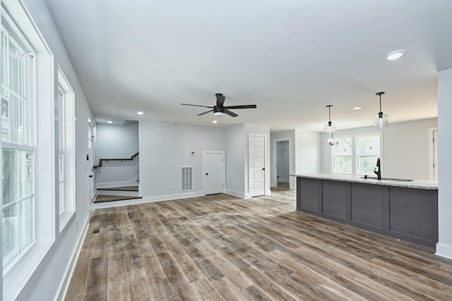 unfurnished living room with sink, ceiling fan with notable chandelier, and hardwood / wood-style flooring