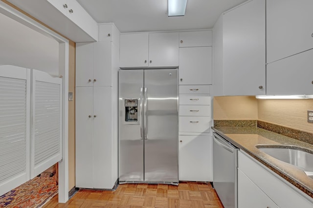 kitchen with decorative backsplash, appliances with stainless steel finishes, light parquet floors, dark stone countertops, and white cabinets