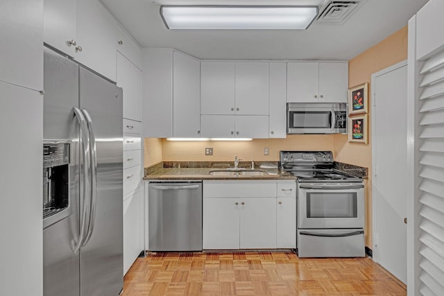 kitchen with light parquet floors, stainless steel appliances, white cabinetry, and sink