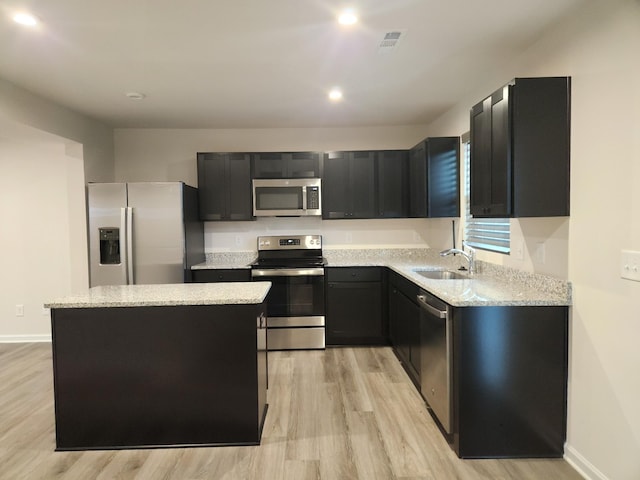 kitchen featuring sink, light stone counters, stainless steel appliances, and a center island