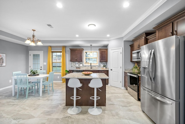 kitchen with light stone countertops, a center island, a notable chandelier, decorative light fixtures, and appliances with stainless steel finishes