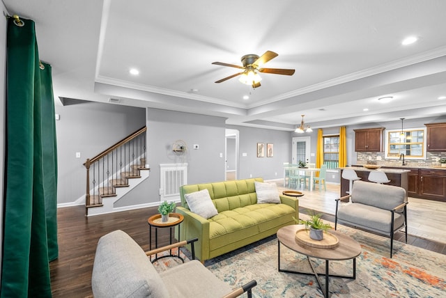 living room with ceiling fan with notable chandelier, dark wood-type flooring, crown molding, and sink