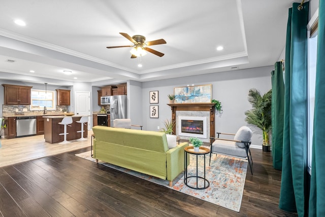 living room featuring a high end fireplace, a raised ceiling, ceiling fan, and dark wood-type flooring