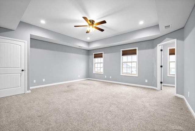 carpeted spare room with a raised ceiling and ceiling fan