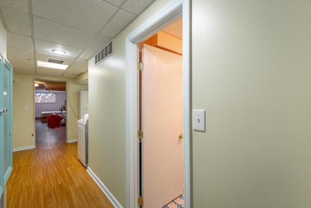 hall with washer / dryer, light hardwood / wood-style flooring, and a drop ceiling