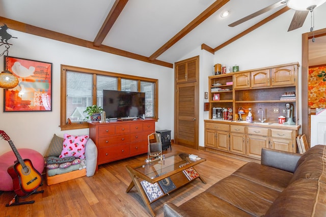 living room featuring ceiling fan, sink, vaulted ceiling with beams, light hardwood / wood-style floors, and a wood stove