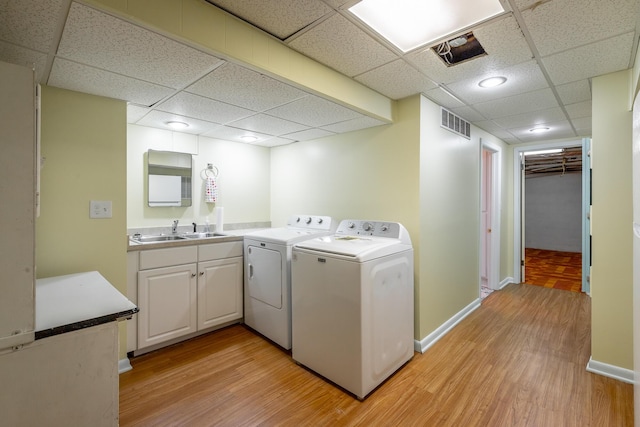 laundry room with washing machine and dryer, cabinets, sink, and light hardwood / wood-style floors