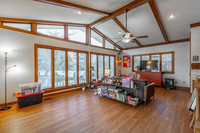 interior space featuring ceiling fan, wood-type flooring, beam ceiling, high vaulted ceiling, and a wood stove