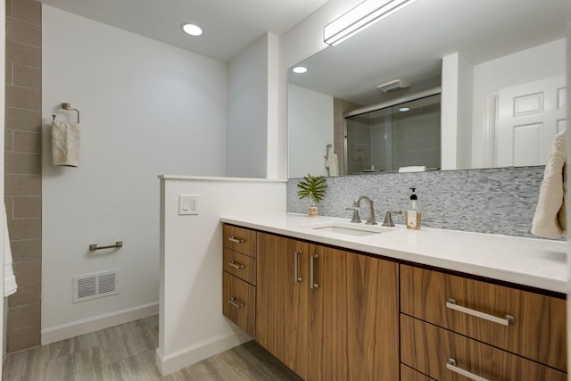 bathroom with backsplash, vanity, wood-type flooring, and a shower with shower door