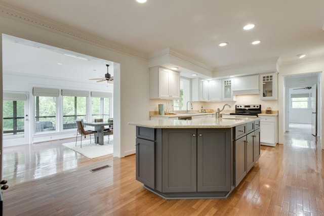 kitchen featuring light stone countertops, gray cabinetry, ceiling fan, a center island with sink, and white cabinets