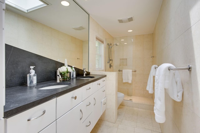 bathroom with a skylight, walk in shower, tile patterned floors, vanity, and tile walls