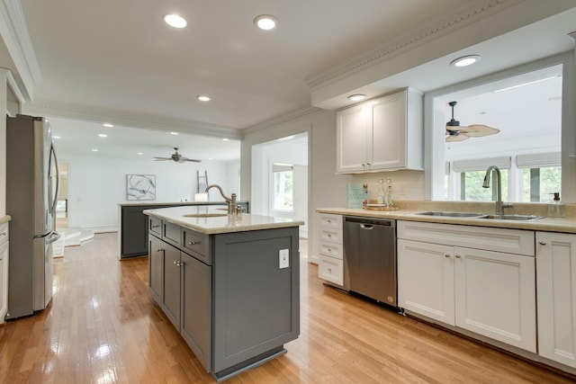 kitchen featuring white cabinets, a center island with sink, sink, ornamental molding, and stainless steel appliances