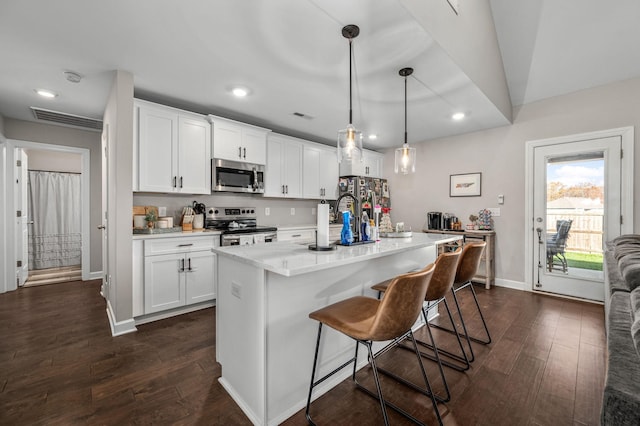 kitchen with white cabinetry, hanging light fixtures, a breakfast bar area, a kitchen island with sink, and appliances with stainless steel finishes