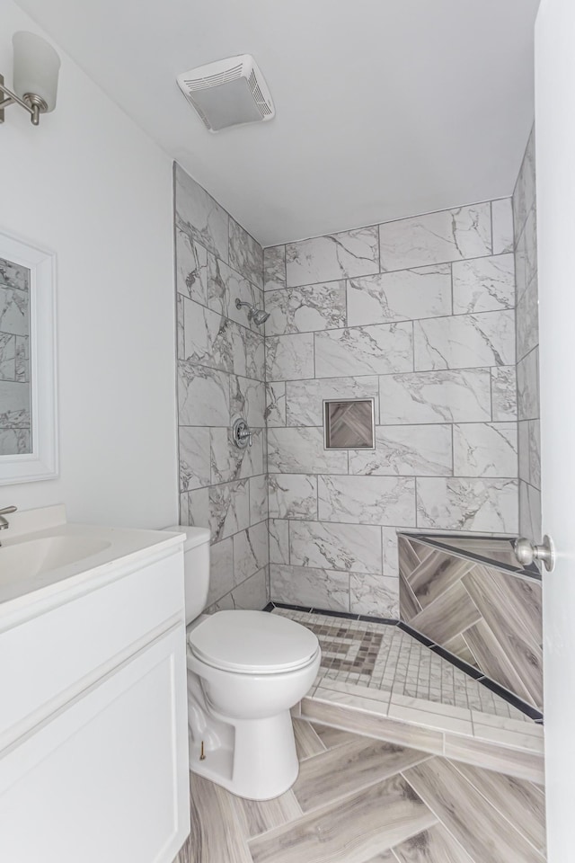 bathroom featuring vanity, toilet, and a tile shower