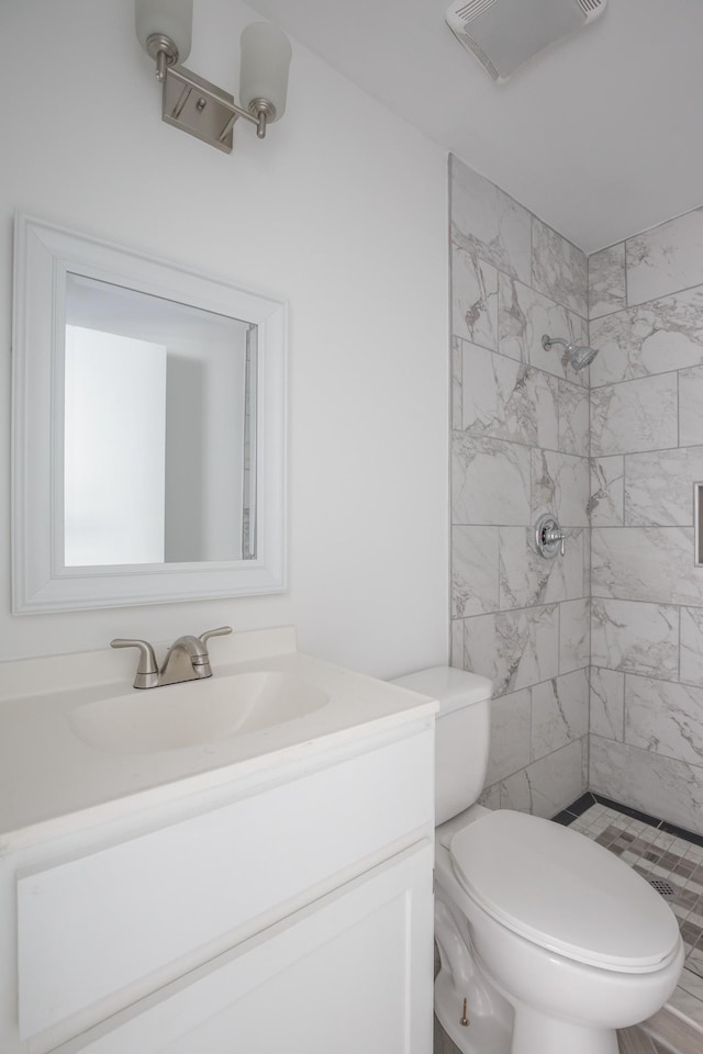 bathroom with toilet, vanity, and tiled shower