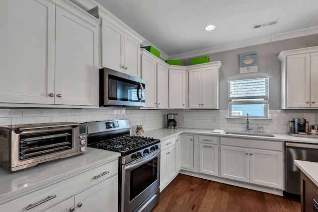 kitchen with appliances with stainless steel finishes, backsplash, dark wood-type flooring, sink, and white cabinets