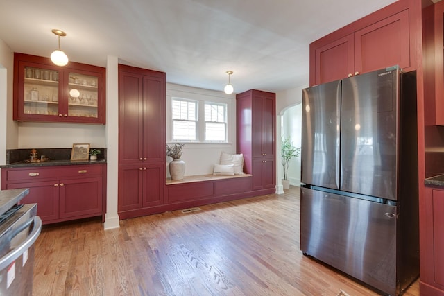 kitchen with stainless steel refrigerator, dark stone countertops, decorative light fixtures, and light wood-type flooring