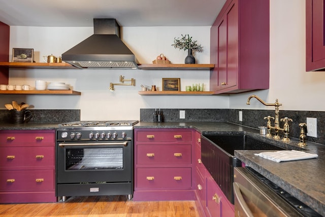 kitchen with appliances with stainless steel finishes, light wood-type flooring, dark stone counters, and wall chimney range hood