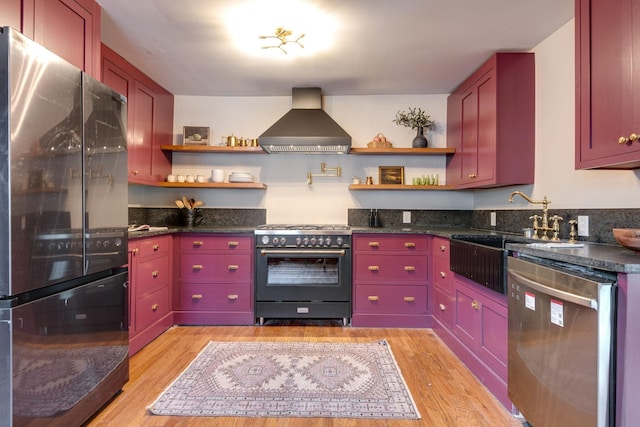 kitchen with appliances with stainless steel finishes, light hardwood / wood-style floors, wall chimney exhaust hood, and sink