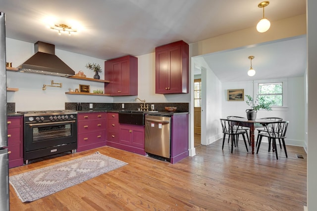 kitchen featuring wall chimney range hood, gas range oven, stainless steel dishwasher, pendant lighting, and light wood-type flooring