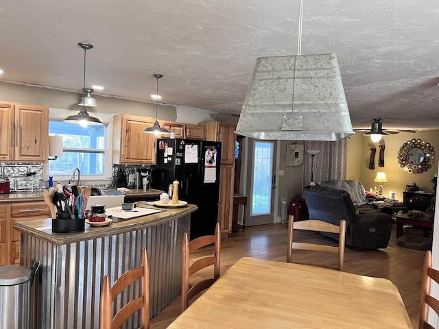 kitchen with a center island, ceiling fan, light wood-type flooring, decorative light fixtures, and black fridge with ice dispenser