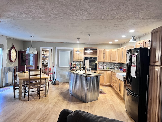 kitchen featuring pendant lighting, backsplash, a kitchen island with sink, and black appliances