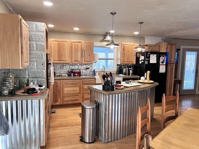 kitchen featuring pendant lighting, black fridge, sink, light hardwood / wood-style flooring, and decorative backsplash