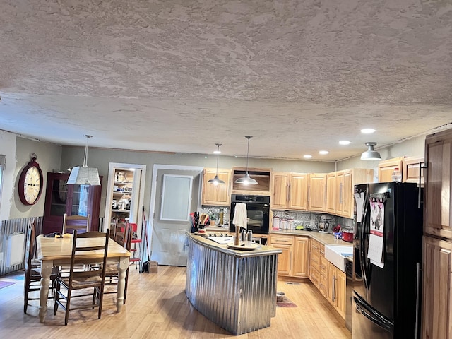 kitchen with black appliances, decorative light fixtures, backsplash, and a kitchen island with sink