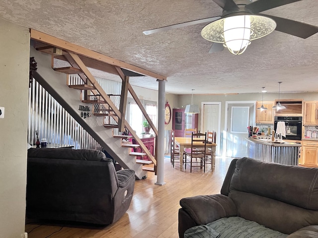 living room featuring ceiling fan, light hardwood / wood-style flooring, and a textured ceiling