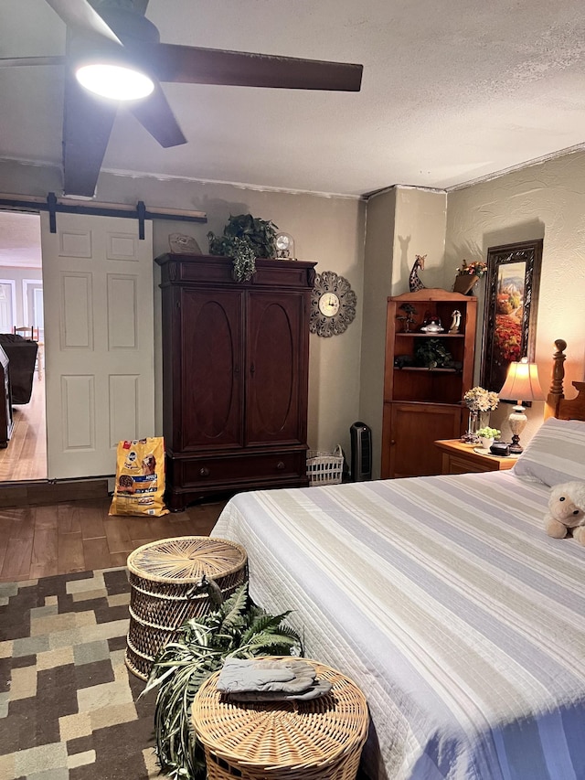 bedroom with a textured ceiling, a barn door, ceiling fan, and dark wood-type flooring