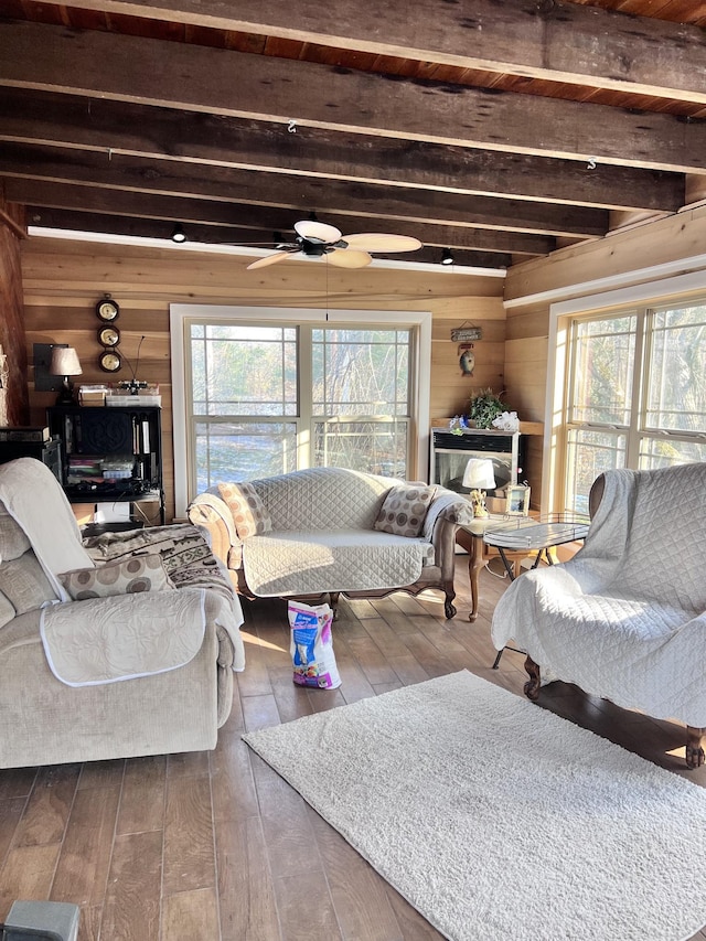 living room featuring beamed ceiling, wood-type flooring, ceiling fan, and wood walls