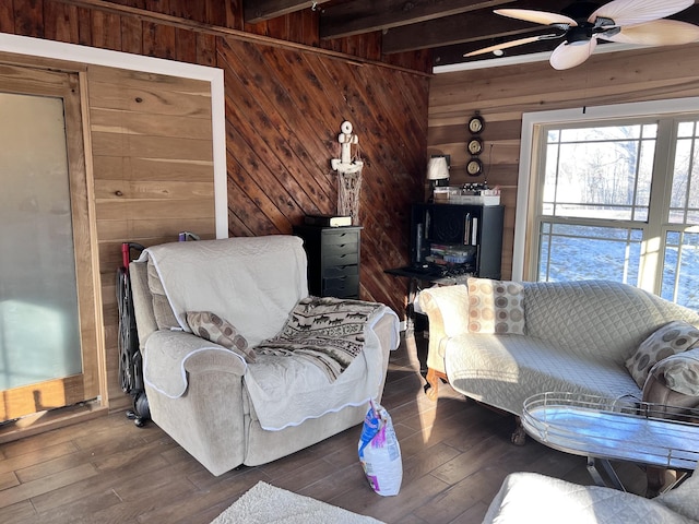 living room featuring wood walls, beamed ceiling, dark wood-type flooring, and ceiling fan