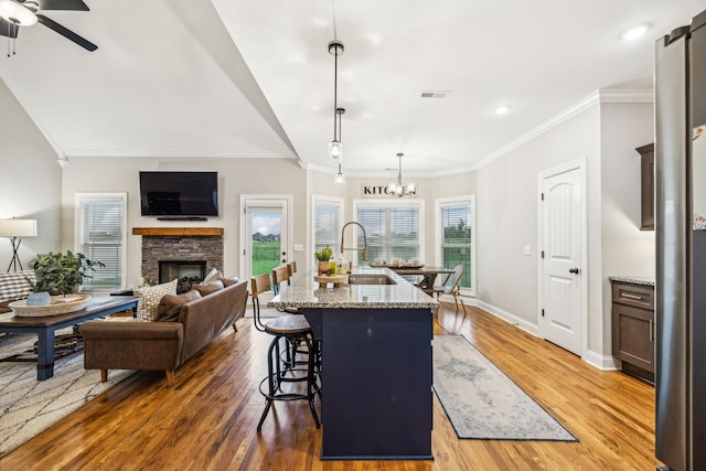 kitchen with decorative light fixtures, light stone counters, a kitchen island with sink, and sink