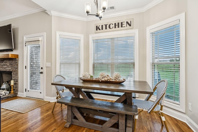 dining room featuring hardwood / wood-style floors, a notable chandelier, a stone fireplace, and crown molding