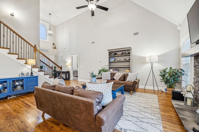 living room featuring hardwood / wood-style flooring, ceiling fan with notable chandelier, a towering ceiling, and ornamental molding