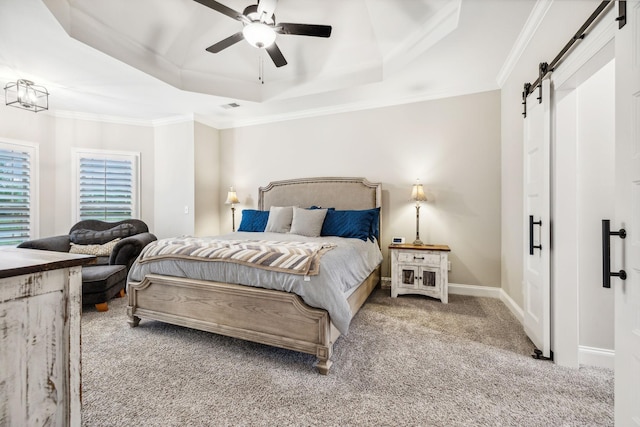 carpeted bedroom with ceiling fan, a barn door, crown molding, and a tray ceiling