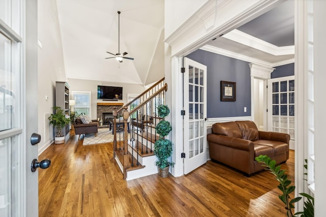 foyer entrance with hardwood / wood-style floors, ceiling fan, a stone fireplace, and ornamental molding