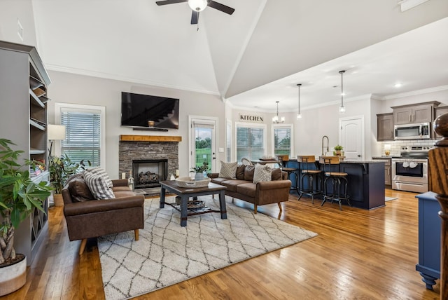 living room with a stone fireplace, light wood-type flooring, lofted ceiling, ceiling fan with notable chandelier, and ornamental molding