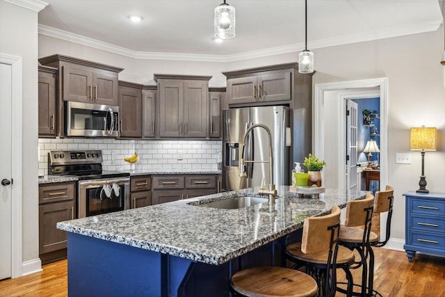 kitchen with dark brown cabinetry, stainless steel appliances, tasteful backsplash, and an island with sink