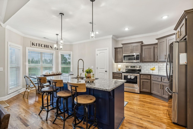 kitchen with a center island with sink, light stone countertops, stainless steel appliances, and hanging light fixtures