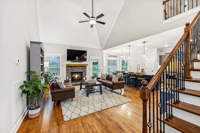 living room featuring wood-type flooring, ceiling fan with notable chandelier, high vaulted ceiling, and a stone fireplace