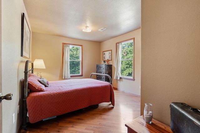 bedroom featuring multiple windows, a textured ceiling, and hardwood / wood-style flooring