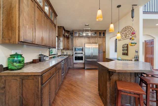 kitchen featuring stainless steel appliances, sink, wood-type flooring, hanging light fixtures, and a breakfast bar area