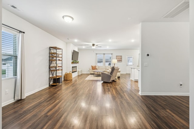 unfurnished living room featuring ceiling fan, a fireplace, and dark wood-type flooring