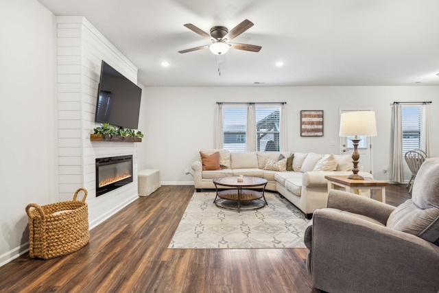 living room with a large fireplace, ceiling fan, and dark wood-type flooring