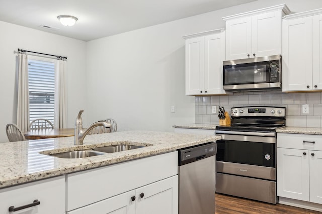 kitchen with backsplash, light stone counters, stainless steel appliances, sink, and white cabinets