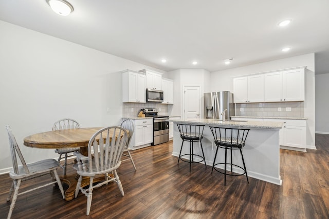 kitchen with decorative backsplash, a kitchen island with sink, white cabinets, and stainless steel appliances